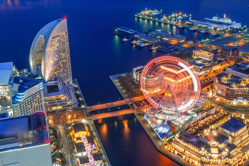 Vista aérea e noturna de Yokohama, com prédios e roda-gigante