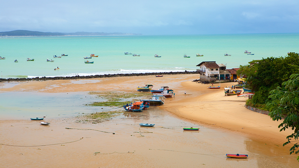 Faixa de areia da Baía Formosa com algumas embarcações atracadas e outras no oceano