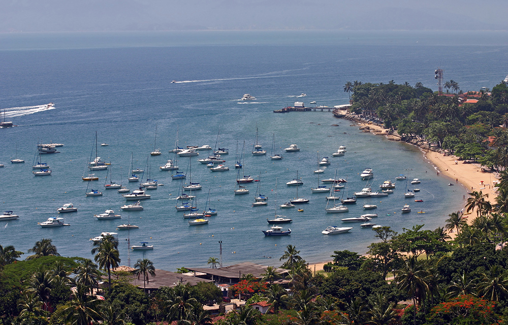 Vista aérea de Ilhabela com barcos na água e mata ao fundo e no primeiro plano