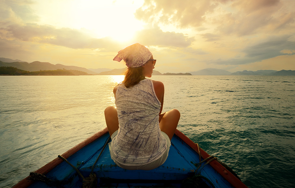 Mulher sentada na ponta de um barco admirando a paisagem