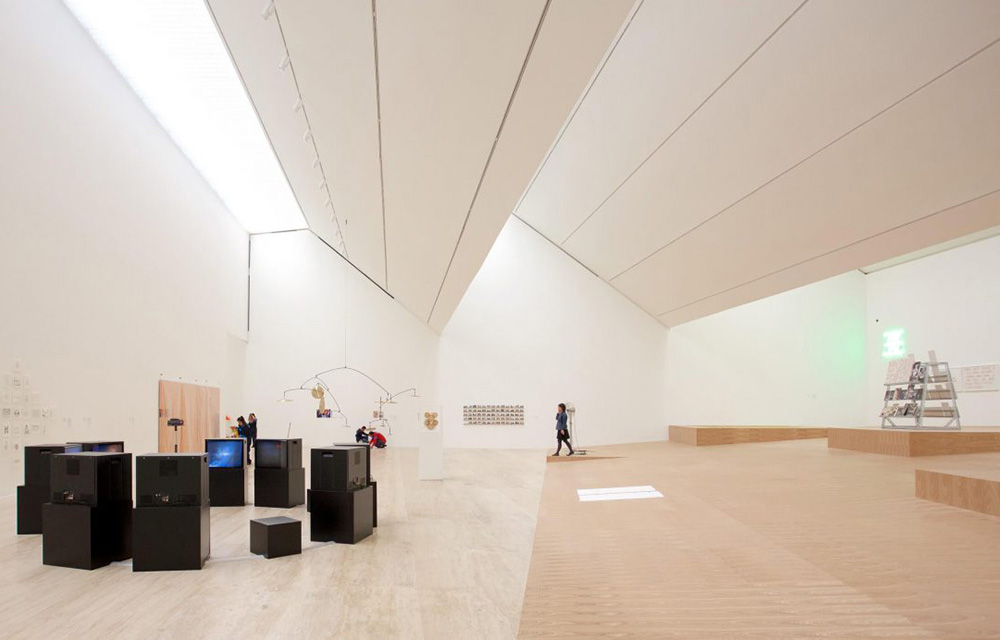 Grande sala branca com caixas pretas à esquerda e uma pessoa ao fundo