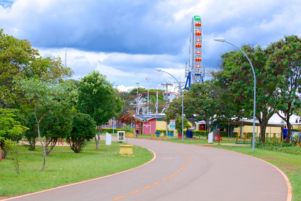 Rua do Parque da Cidade com uma roda gigante e uma montanha-russa ao fundo