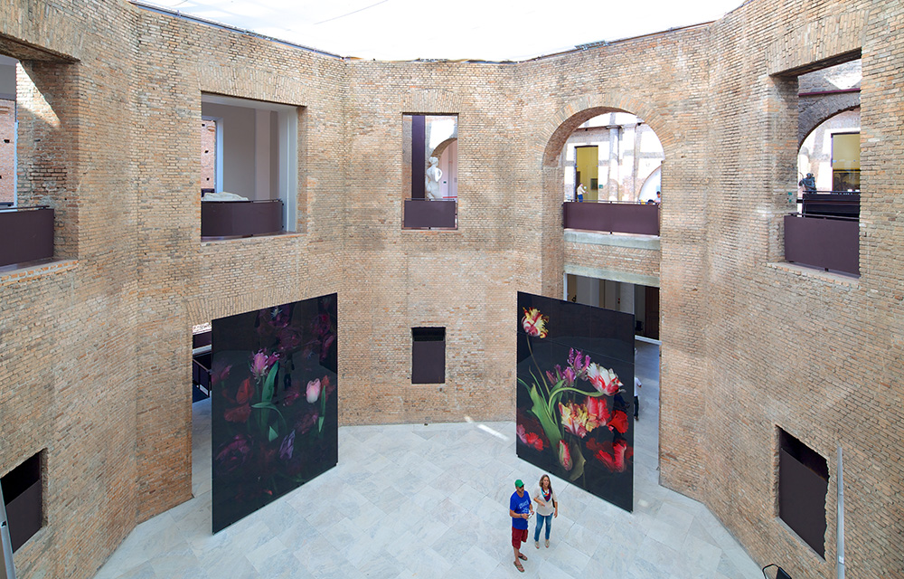 Vista do alto da galeira central da Pinacoteca com dois grandes quadros ao fundo e pessoas observando as obras.