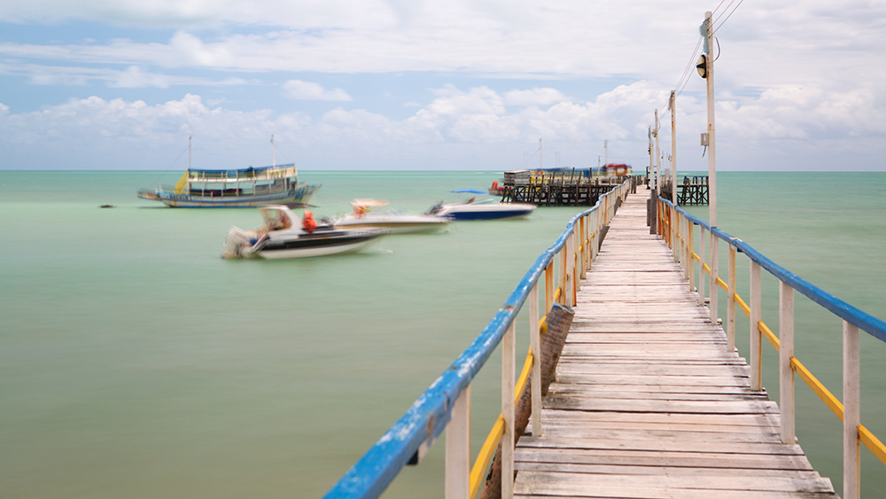Píer em direção ao horizonte com embarcações no mar