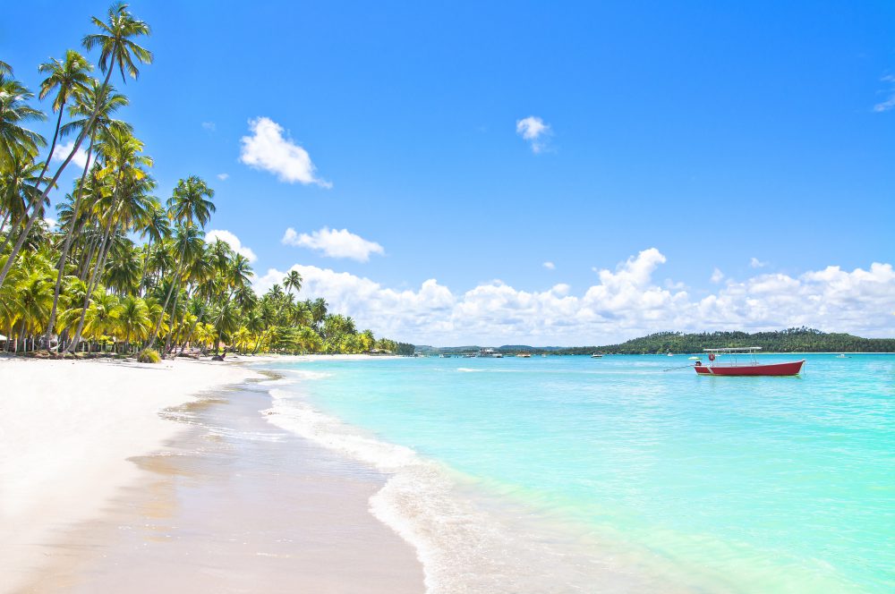 Vista lateral da Praia dos Carneiros com um barco vermelho na água