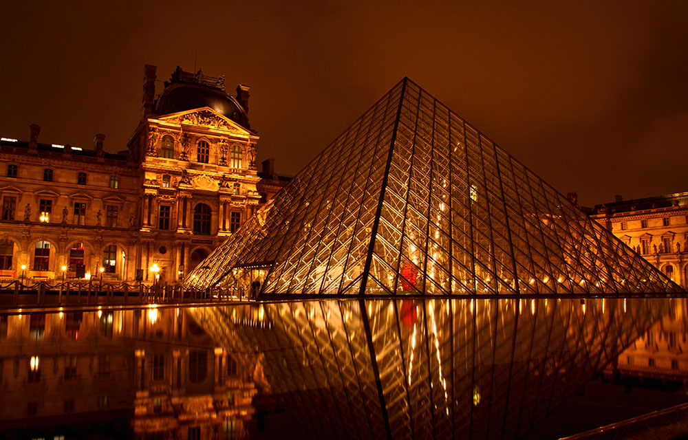 Pirâmide do Museu do Louvre com Museu ao fundo, à noite