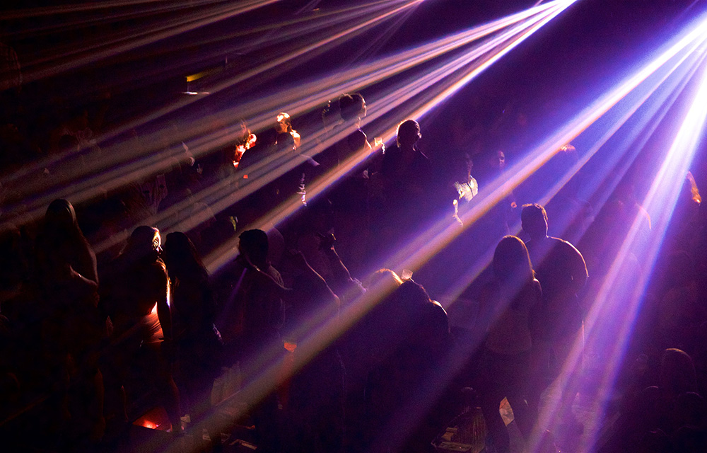 Pessoas dançando em uma boate com luzes cortando a imagem